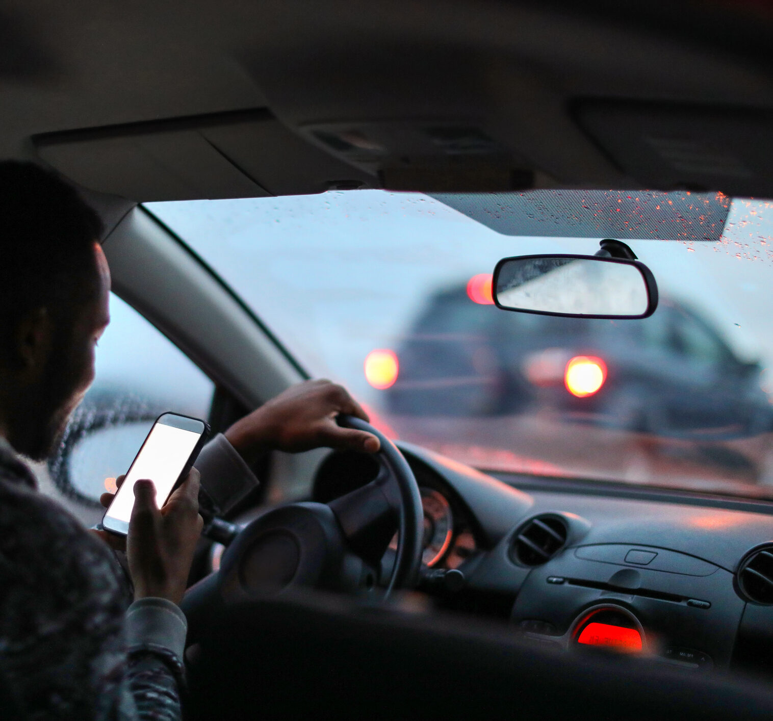 man using his phone while driving in the rain.