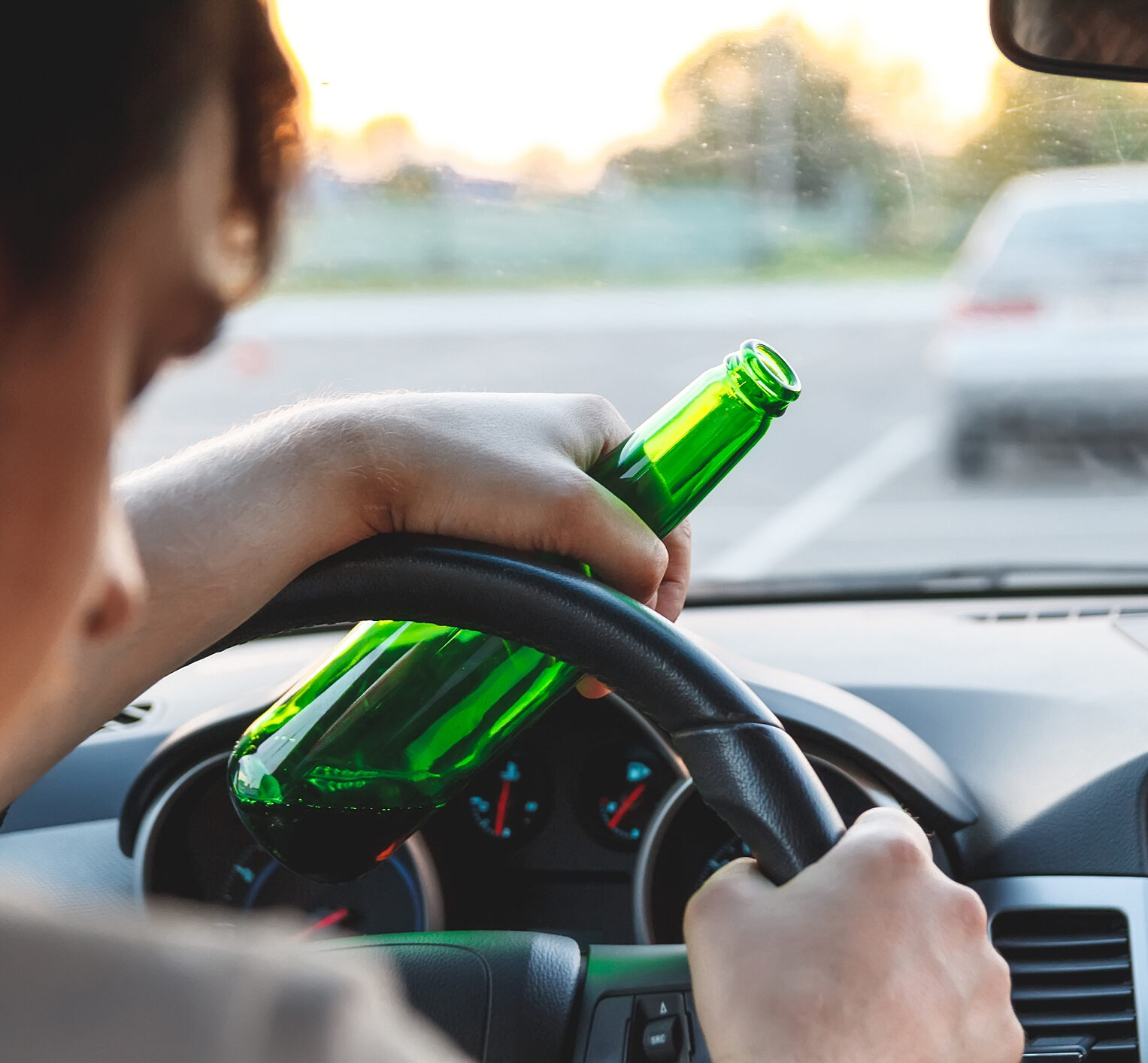 A man driving a car with a bottle of beer